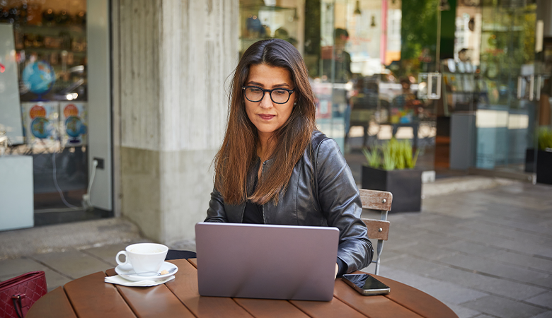 Eine Frau sitzt mit ihrem Laptop in einem Straßencafé an einem Tisch.