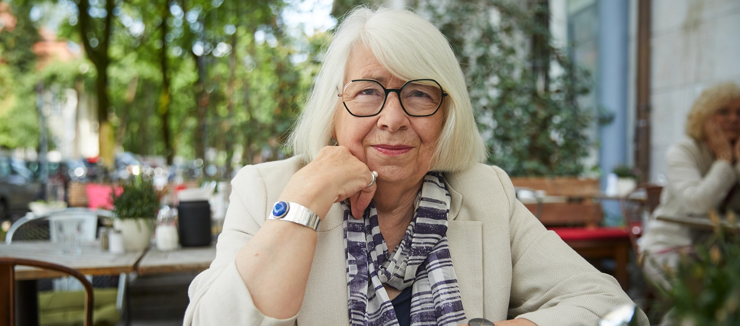 Eine Frau mit einer Brille sitzt an einem Tisch und schaut in die Kamera.