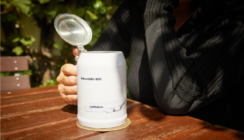 Ein Bierglas mit der Aufschrift Airbus steht auf einem Holztisch. Eine Hand greift danach. 