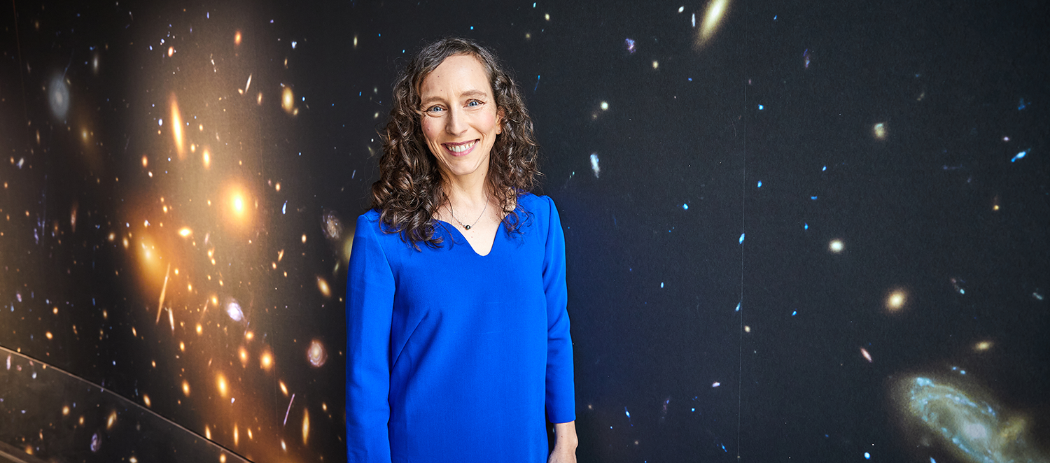 Eine Frau steht vor einer Sternentapete und lächelt. 