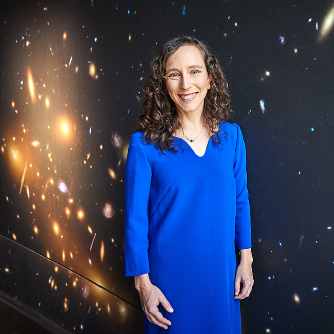 Eine Frau steht vor einer Sternentapete und lächelt. 