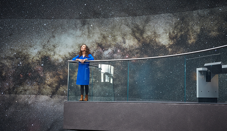 Eine Frau steht an einer Brüstung in einer Ausstellung zu Sternen und schaut nach oben. 