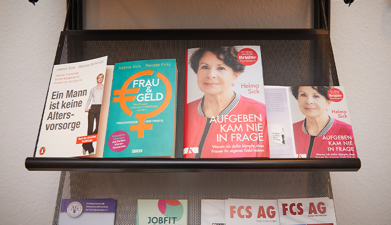 In einem Regal liegen Broschüren zum Thema Frauen und Geld. 