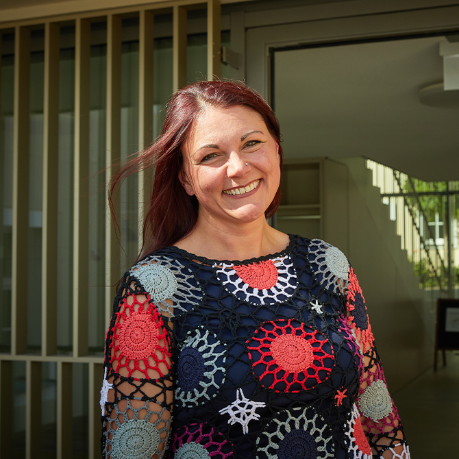 Eine Frau steht vor einem Hauseingang und lächelt.