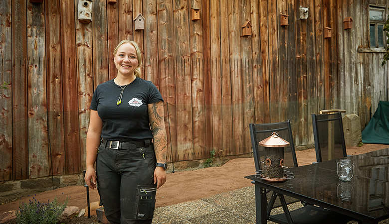 Eine Frau in Handwerkskleidung steht vor einer Scheune. 