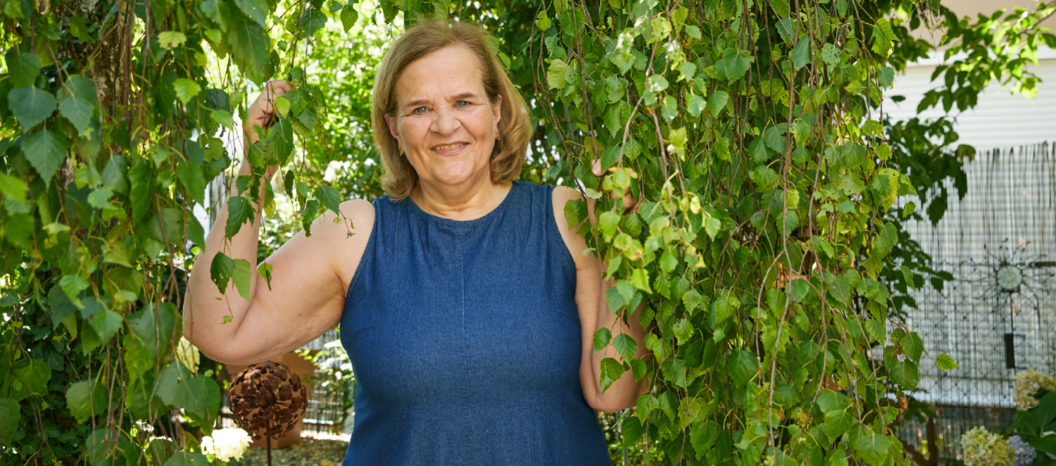 Eine Frau in einem Sommerkleid steht unter einem Baum mit Efeu.