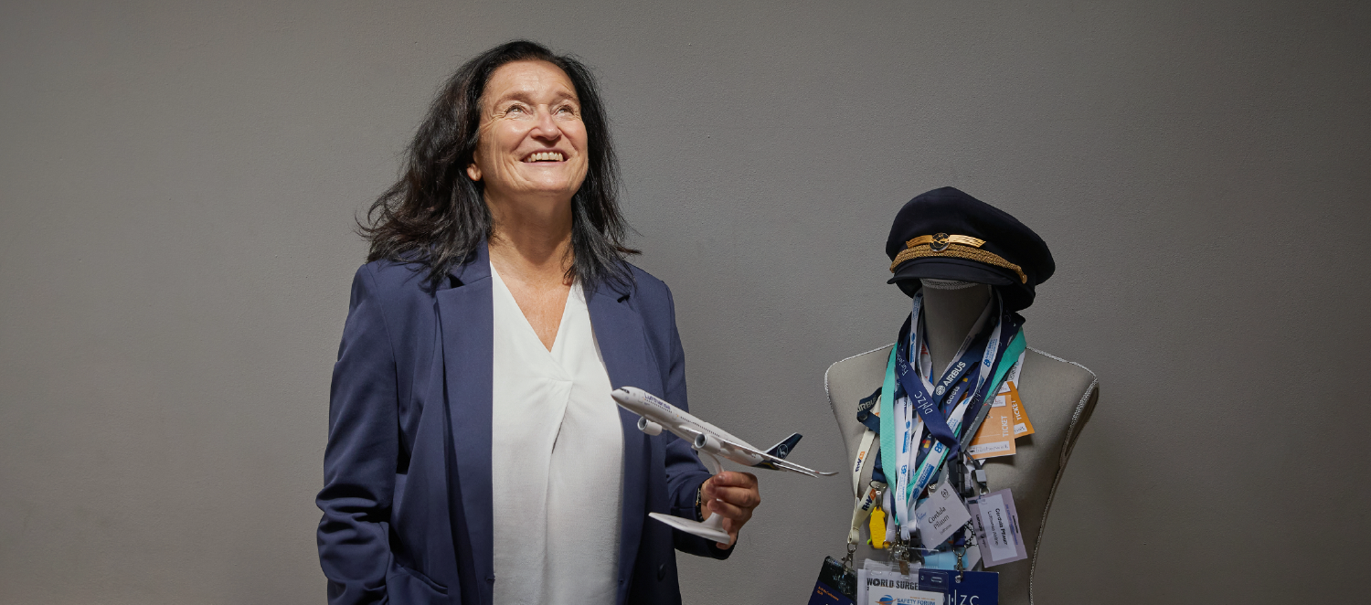 Eine Frau steht mit einem Spielzeugflugzeug in der Hand in einem Raum und schaut nach oben.