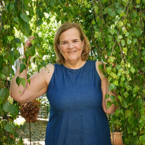 Eine Frau in einem Sommerkleid steht unter einem Baum mit Efeu. 