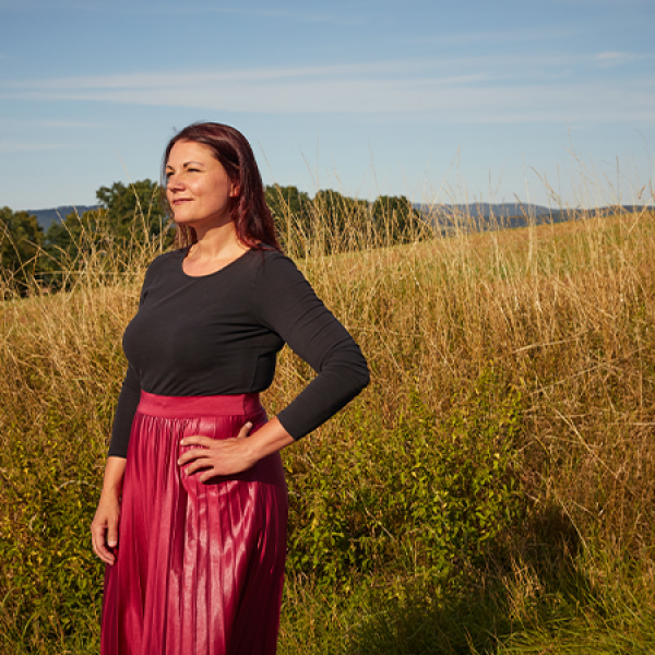 Eine Frau steht an einem Feldweg und blickt in die Ferne.  
