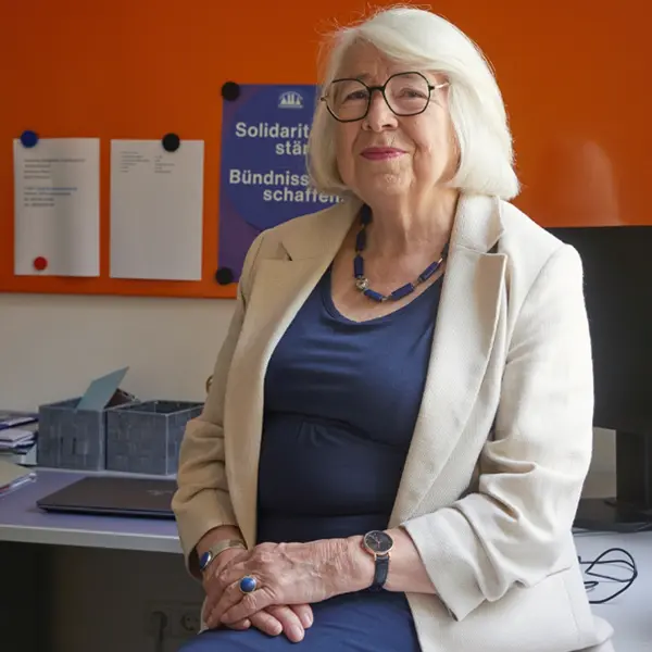 Eine Frau sitzt auf einem Tisch, im Hintergrund ist der Arbeitsplatz mit einem Computer zu sehen.  