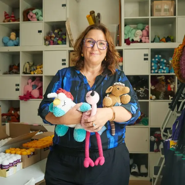 Eine Frau hält Kuscheltiere im Arm. Hinter ihr ist ein Regal mit Stricksachen. 