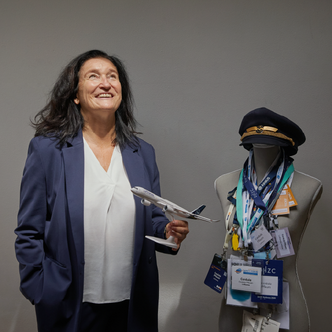 Eine Frau steht mit einem Spielzeugflugzeug in der Hand in einem Raum und schaut nach oben.