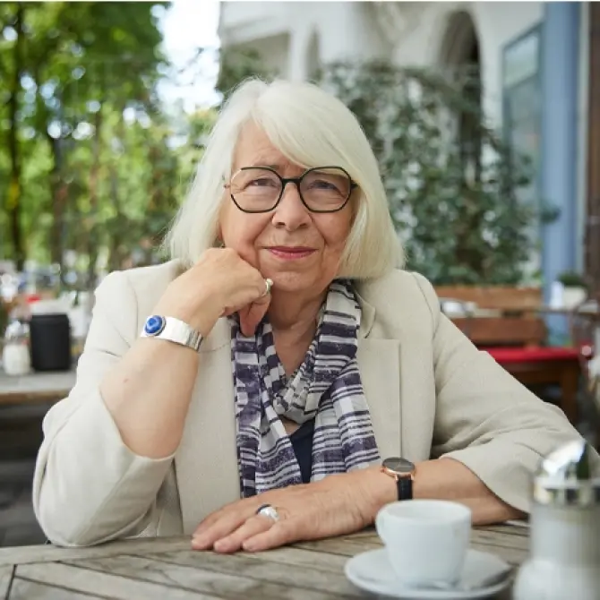 Eine Frau sitzt an einem Tisch und schaut in die Kamera.