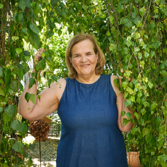 Eine Frau in einem Sommerkleid steht unter einem Baum mit Efeu.