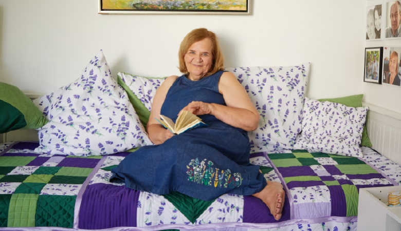 Eine Frau liegt auf einem Bett mit vielen Kissen am Kopf und einem Buch in den Händen.