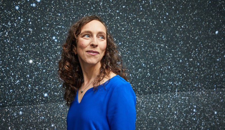 Eine Frau steht vor einer Sternentapete und schaut zur Seite. 