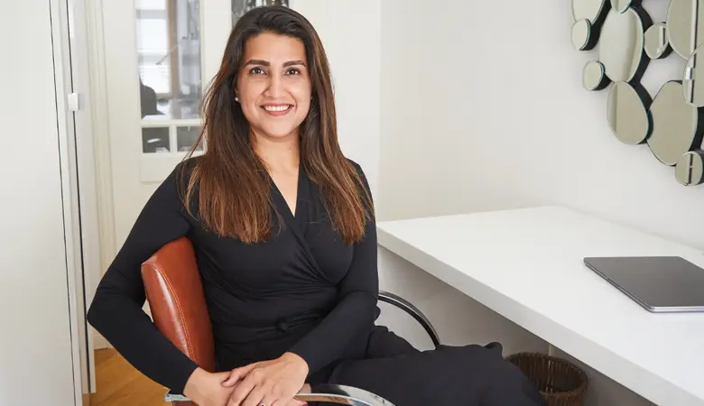 Eine Frau sitzt auf einem Stuhl am Schreibtisch und schaut in die Kamera. 