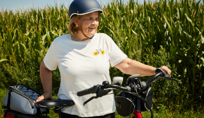 Eine Frau steht mit ihrem Fahrrad vor einem Maisfeld. 