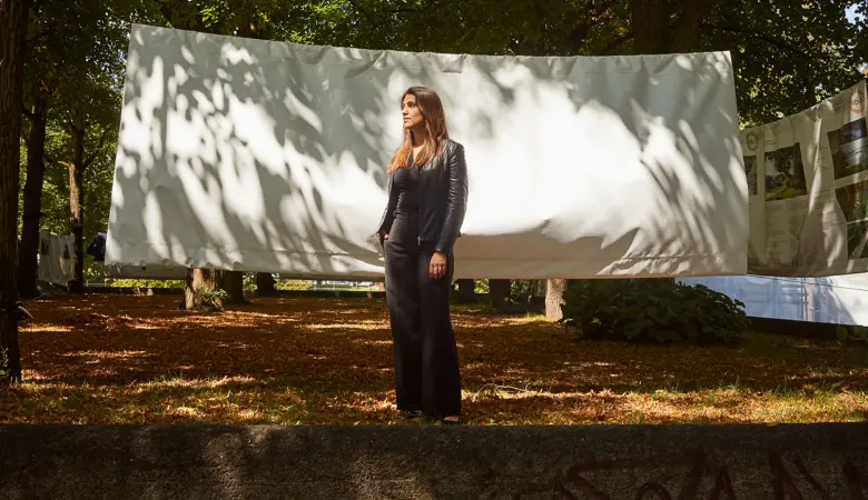 Eine Frau steht auf einem parkähnlichen Gelände mit einer aufgespannten Plane im Hintergrund. 