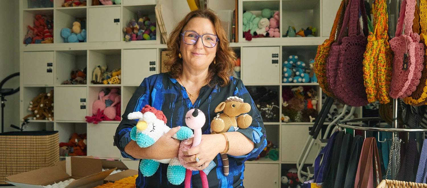 Eine Frau hält Kuscheltiere im Arm. Hinter ihr ist ein Regal mit Stricksachen.