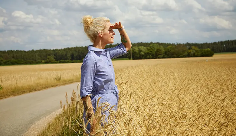 Frau steht im Kornfeld und blickt in die Ferne. 