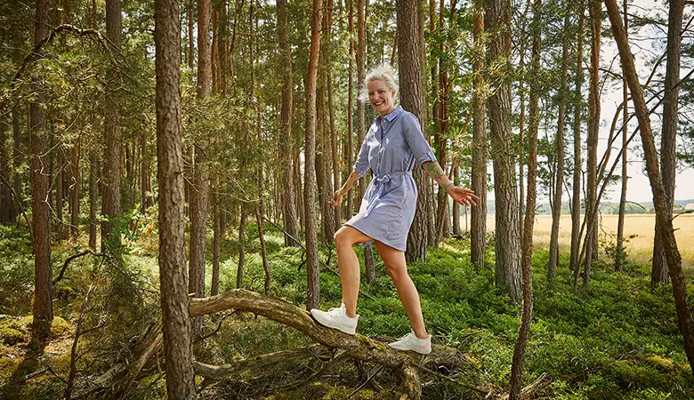 Frau balanciert auf einem umgestürzten Baum im Wald.