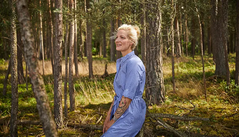 Frau sitzt auf einem Baumstumpf im Wald.