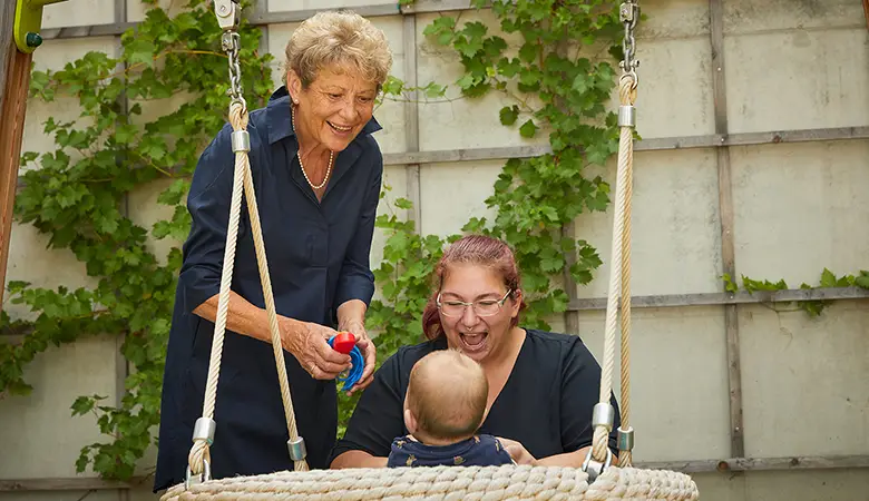 Zwei Frauen stehen an einer Schaukel mit einem Baby. 