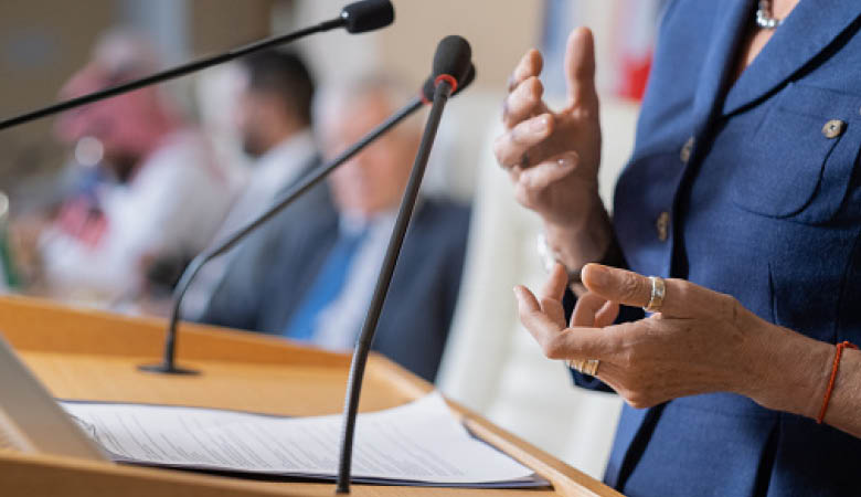 Eine Frau steht am Rednerpult. Sie gestikuliert mit den Händen.