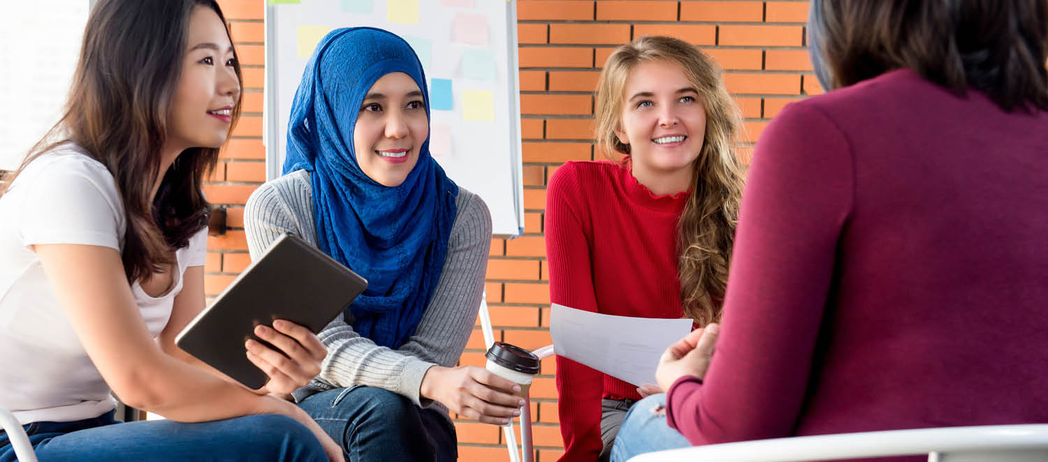 In einem Raum mit Flipchart: Eine diverse Gruppe junger Frauen sitzt im Kreis und diskutiert angeregt. 