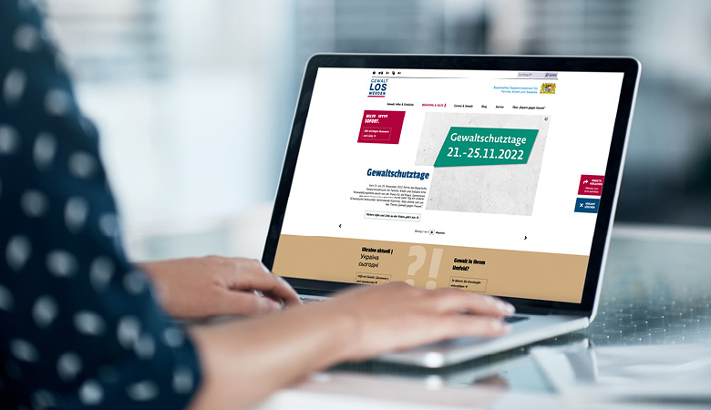 Eine Frau sitzt vor einem Notebook. Sie hat die Website „Bayern gegen Gewalt“ aufgerufen.