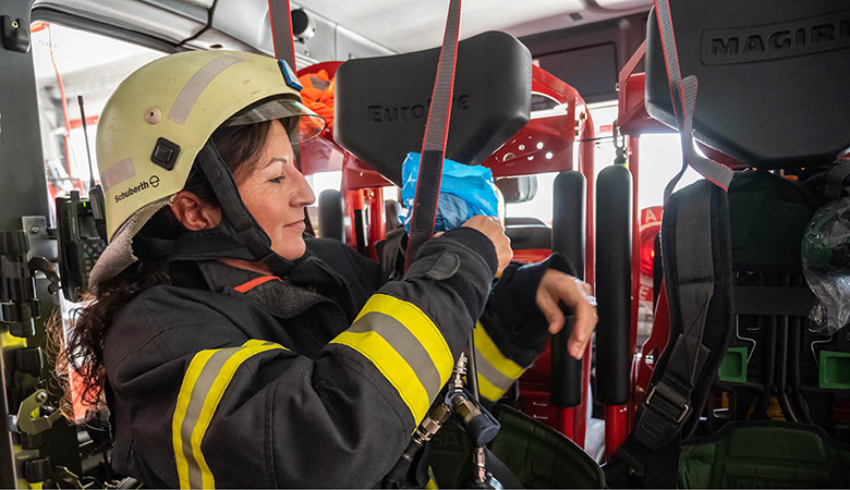 Andrea Fürstberger sitzt mit Helm und Schutzjacke im Einsatzfahrzeug und legt das Atemschutzgerät an.