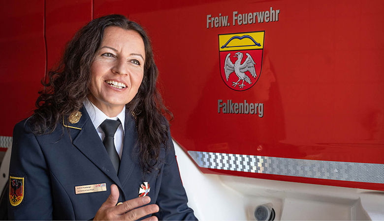Porträtfoto: Andrea Fürstberger in Uniform. Sie steht vor einem Fahrzeug mit dem Logo der Freiwilligen Feuerwehr Falkenberg.