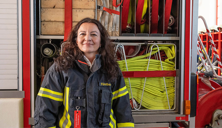 Andrea Fürstberger steht vor einem Einsatzfahrzeug, hinter ihr ist ein zusammengelegter Löschschlauch verstaut.