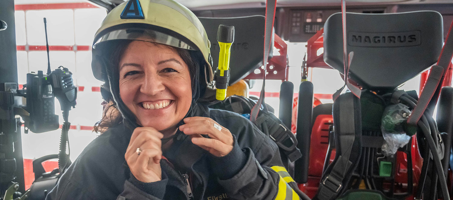 Porträtfoto: Andrea Fürstberger in Einsatzjacke und Helm in einem Feuerwehrfahrzeug.  