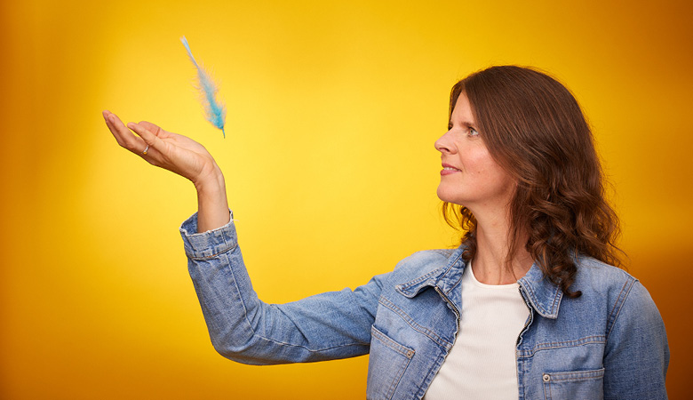Profilfoto: Eine bunte Feder fällt auf Daniela Nuber-Fischers erhobene Handfläche.