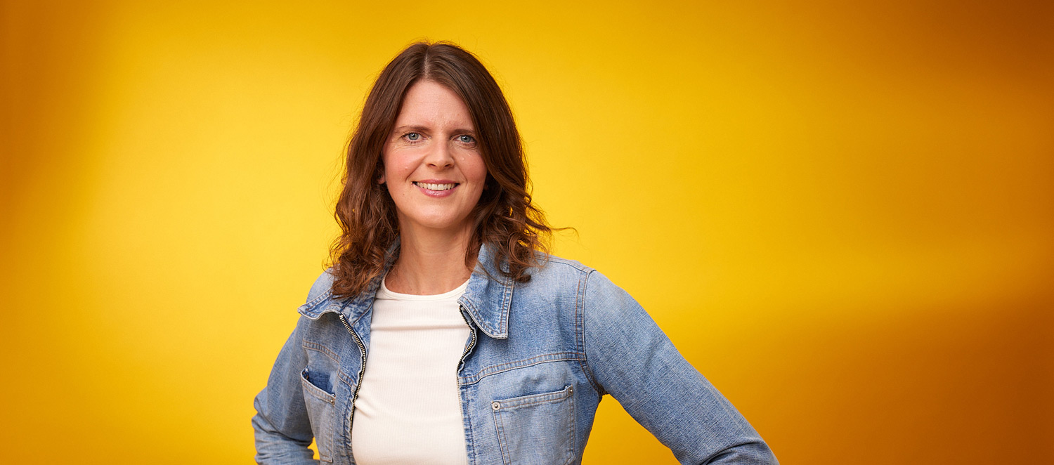 Porträtfoto: Daniela Nuber-Fischer. Sie hat schulterlange braune Haare und trägt T-Shirt, Jeansjacke und einen grünen Rock. 