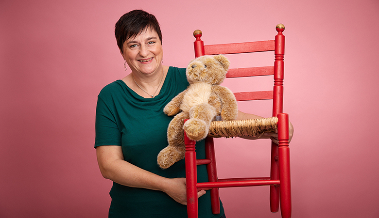 Anja Preuster hebt einen knallroten Kinderstuhl hoch; darauf sitzt ein kuscheliger Teddybär.