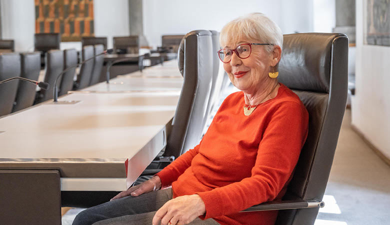 Elisabeth Brock sitzt auf einem Konferenzstuhl in einem Sitzungssahl.