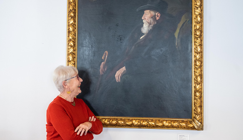 Elisabeth Brock blickt zum Mann auf dem Gemälde und lacht.