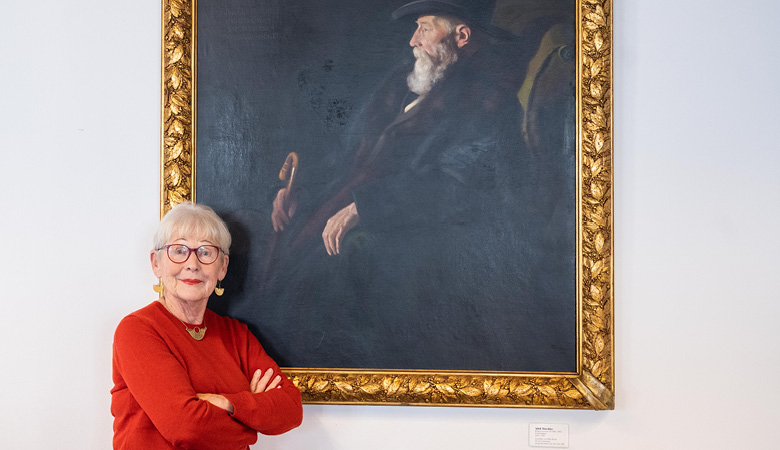 Elisabeth Brock steht vor einem großen, dunkel gehaltenen Gemälde. Es zeigt einen Würdenträger mit grauem Bart.