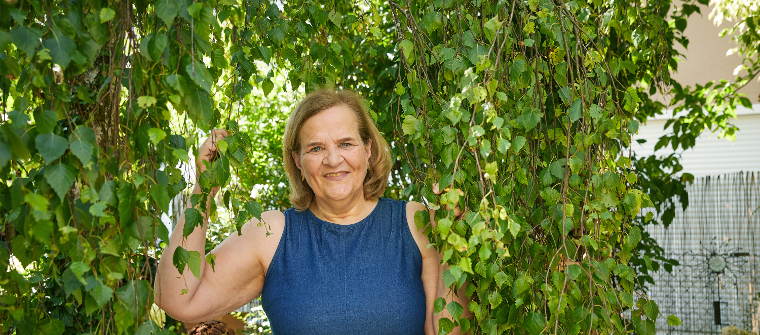 Eine Frau in einem Sommerkleid steht unter einem Baum mit Efeu. 