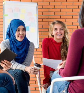 In einem Raum mit Flipchart: Eine diverse Gruppe junger Frauen sitzt im Kreis und diskutiert angeregt.