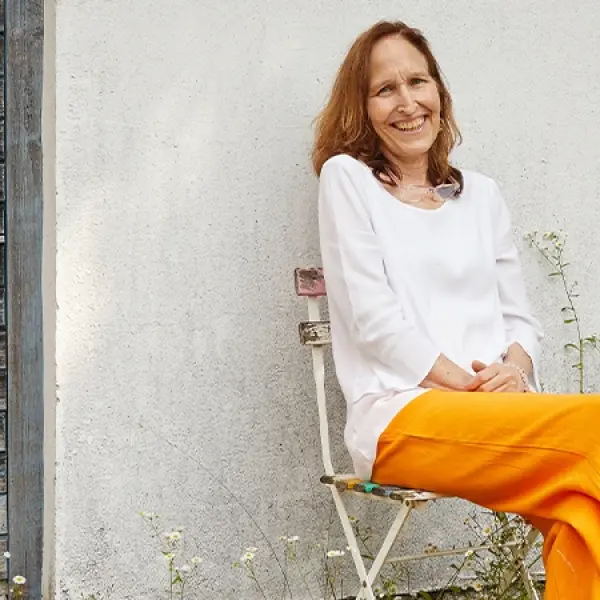 Eine Frau sitzt vor einem Haus auf einem Gartenstuhl. 