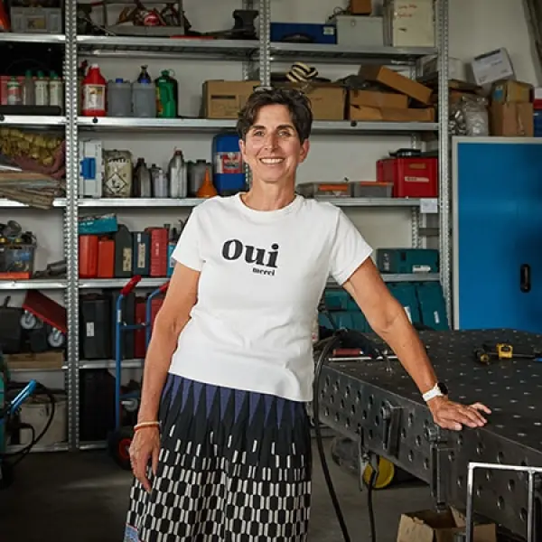 Eine Frau steht in einer Werkstatt an einer Werkbank angelehnt. 