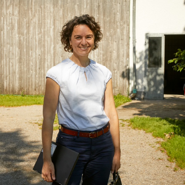 Eine Frau steht vor einer Scheune und lächelt.