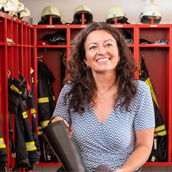 Andrea Fürstberger zieht ihre Einsatzstiefel an. Im Hintergrund sind die Spinde zu sehen, darüber ein Info-Monitor.