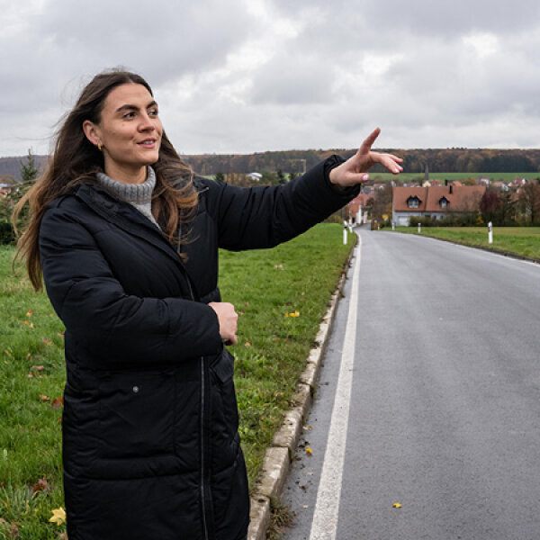 Lisa-Marie Schmitt steht am Straßenrand und deutet auf die Landschaft.