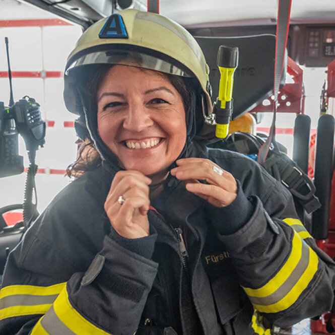 Porträtfoto: Andrea Fürstberger in Einsatzjacke und Helm in einem Feuerwehrfahrzeug.  