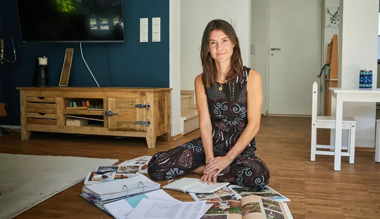 Eine Frau sitzt auf dem Boden in einem Wohnzimmer mit ausgebreiteten Katalogen vor sich. 